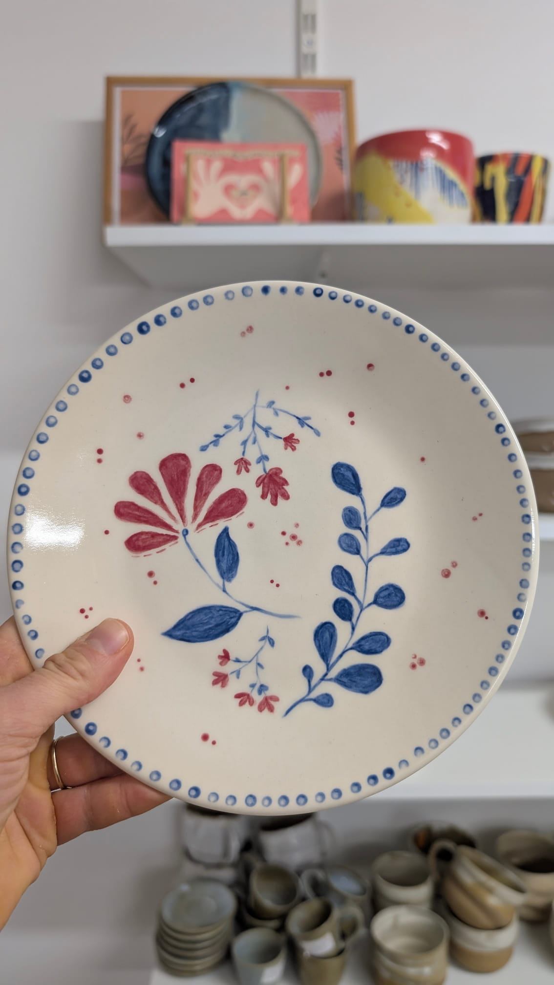 Talerz ceramiczny z motywem florystycznym – czerwony kwiat i niebieskie liście z ozdobną kropkowaną obwódką.