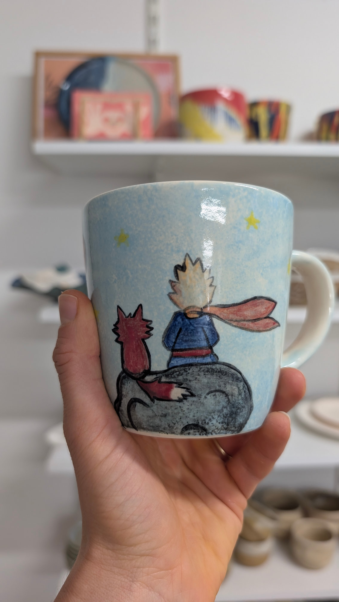 Błękitny kubek z ręcznie malowaną ilustracją Małego Księcia i lisa siedzących na planecie pod gwiazdami.