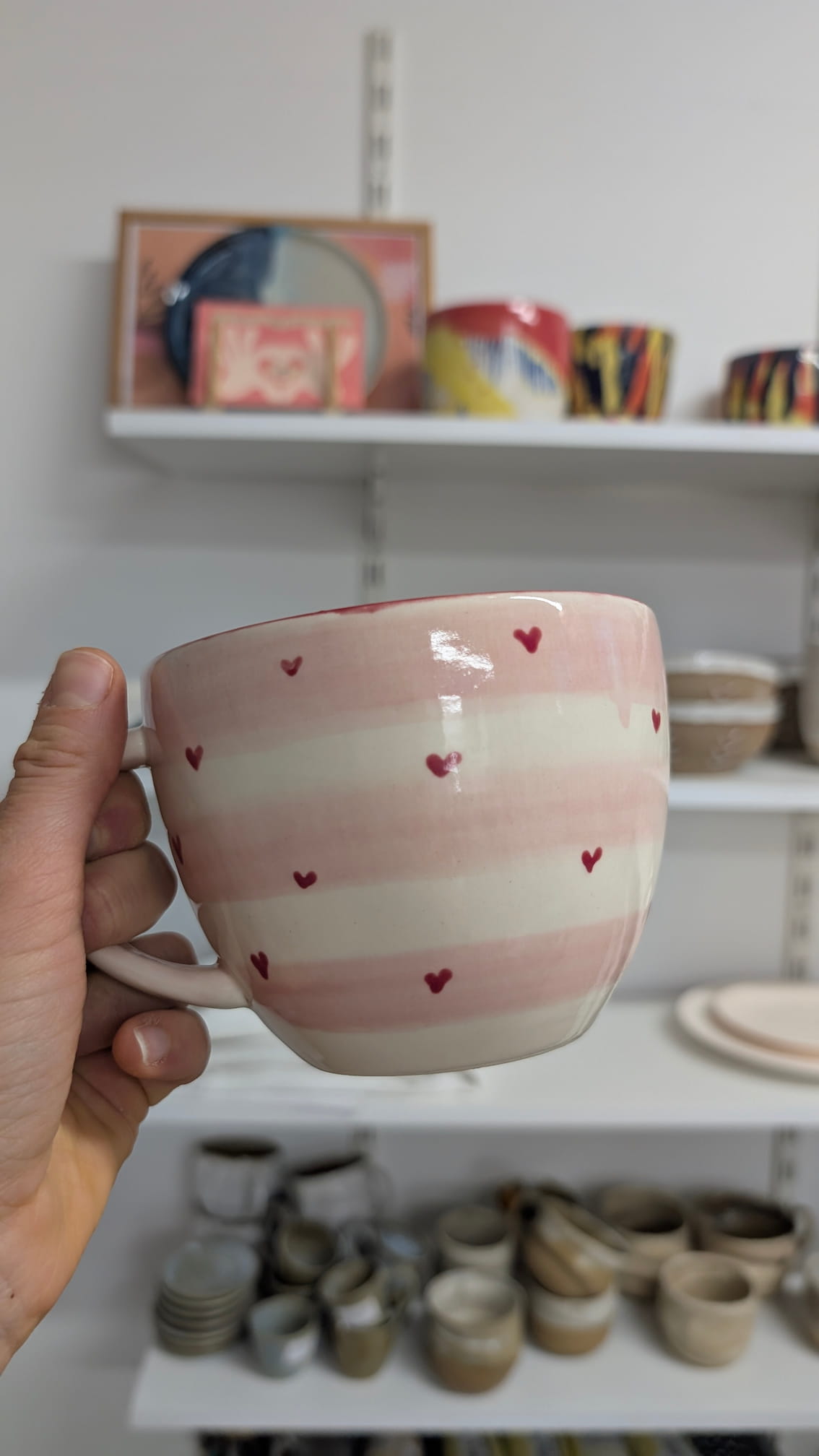Różowy kubek w paski ozdobiony małymi czerwonymi serduszkami – ręcznie malowana ceramika walentynkowa.