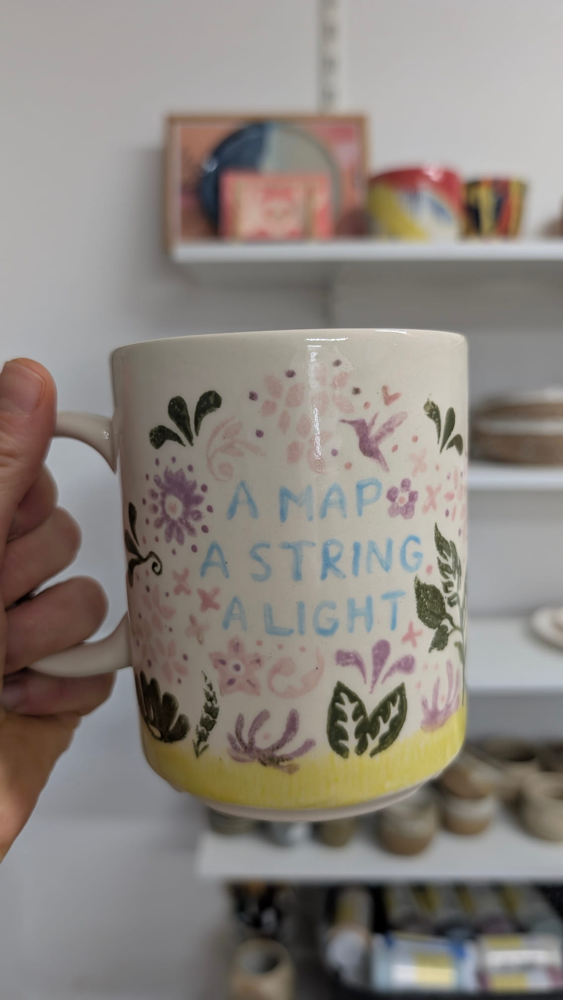 Ręcznie malowany kubek ceramiczny z motywem roślinnym i cytatem A Map A String A Light, ozdobiony delikatnymi kwiatami i ptakiem.