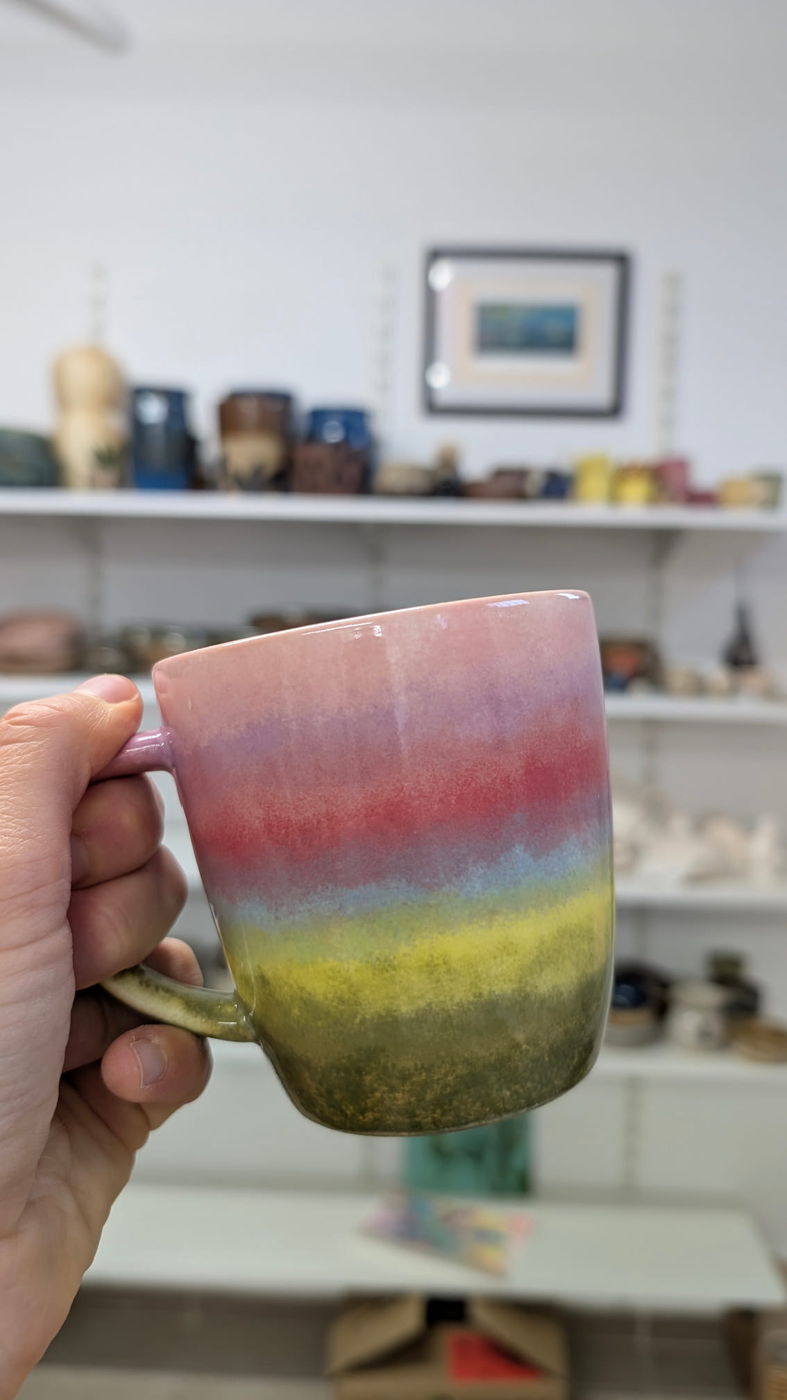 Ceramiczne walentynki 9 Ceramiczny kubek o prostej formie, ozdobiony poziomymi pasami kolorów przechodzącymi płynnie jeden w drugi (efekt ombre). Od góry kolory zmieniają się od bladego różu, przez nasyconą czerwień, błękit i żółć, aż po ciemną, mszystą zieleń na dole.